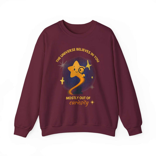A maroon sweatshirt with a graphic of a star looking through a magnifying glass and text about curiosity.