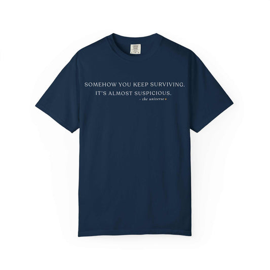 Navy blue Comfort Colors t-shirt with white text 'Somehow you keep surviving. It’s almost suspicious.'