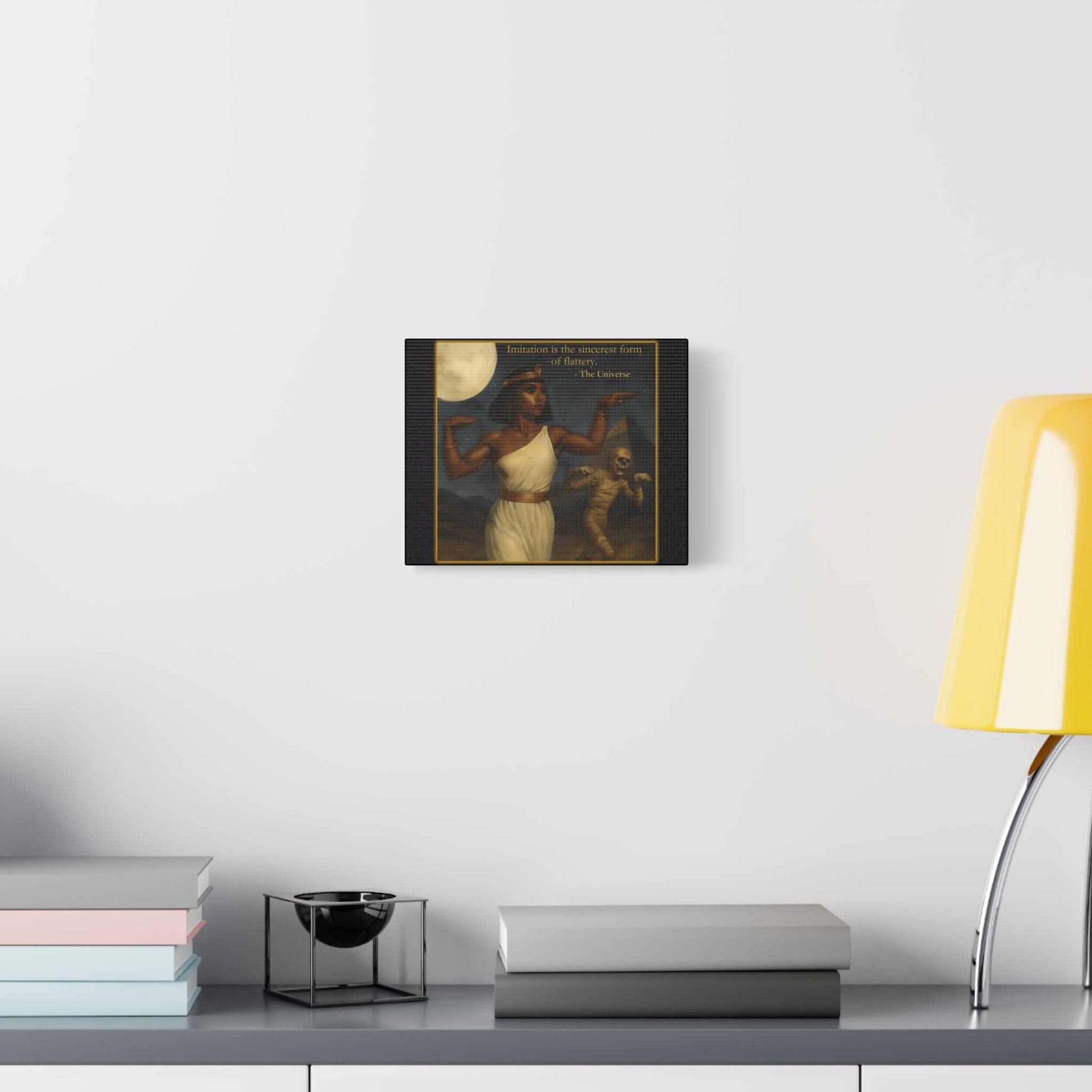 Modern wall art showing a woman in white with mythological figure, displayed above a desk with books and a yellow lamp, Youniverses home decor.