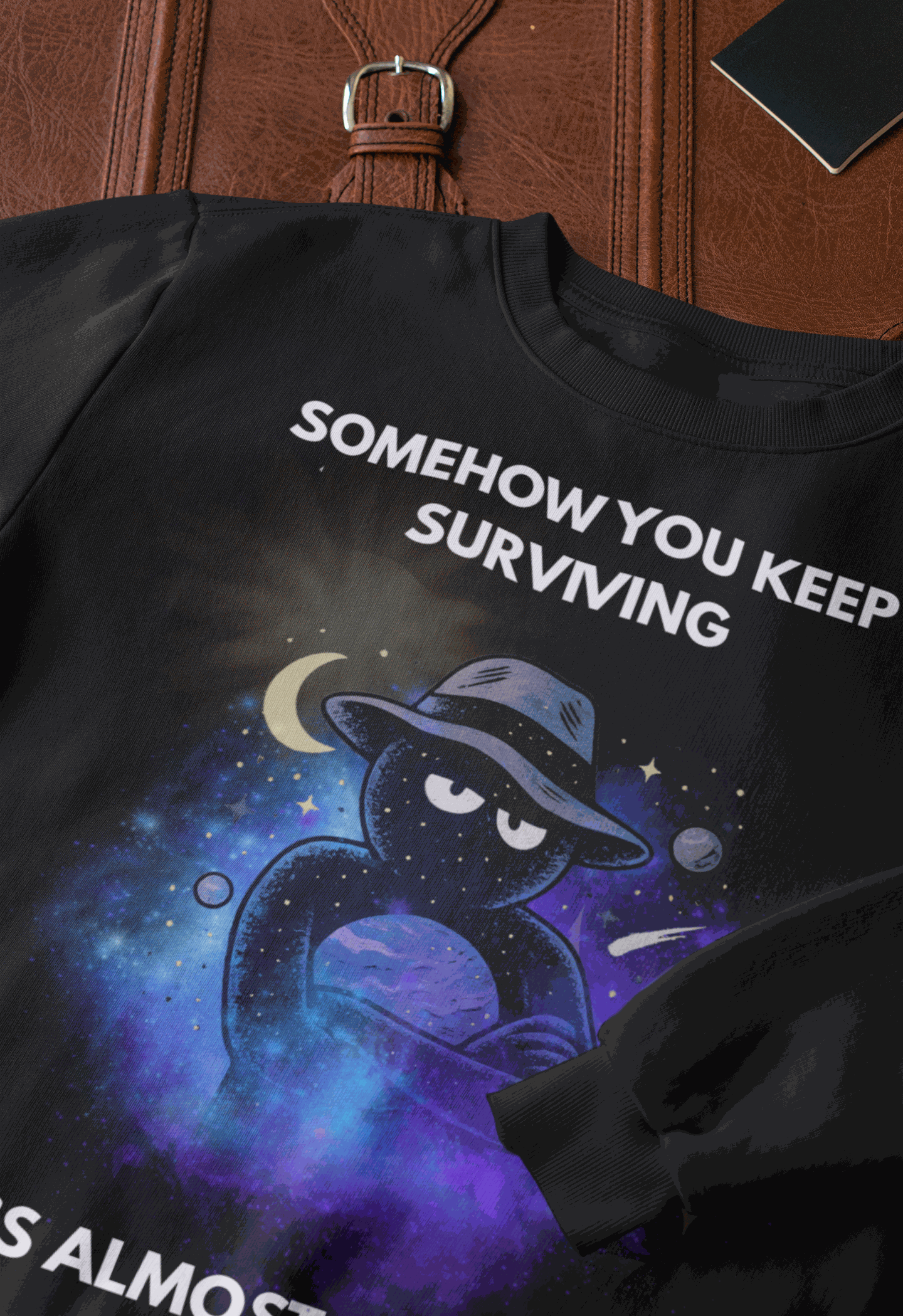 Black sweatshirt with "Somehow You Keep Surviving" text and a cosmic graphic.