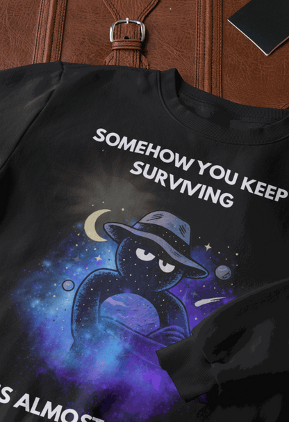 Black sweatshirt with "Somehow You Keep Surviving" text and a cosmic graphic.
