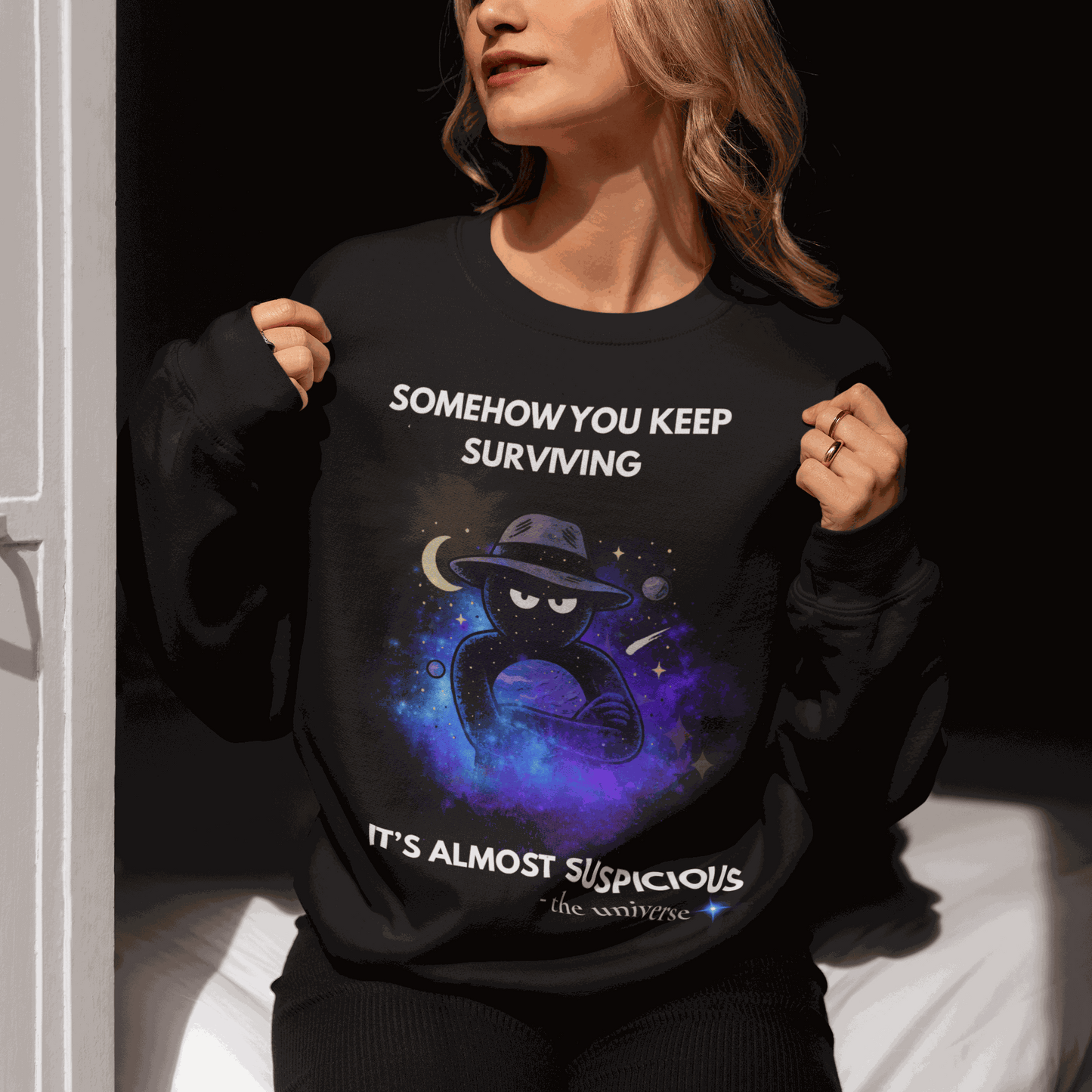Black sweatshirt with "Somehow You Keep Surviving" text and a cosmic graphic.