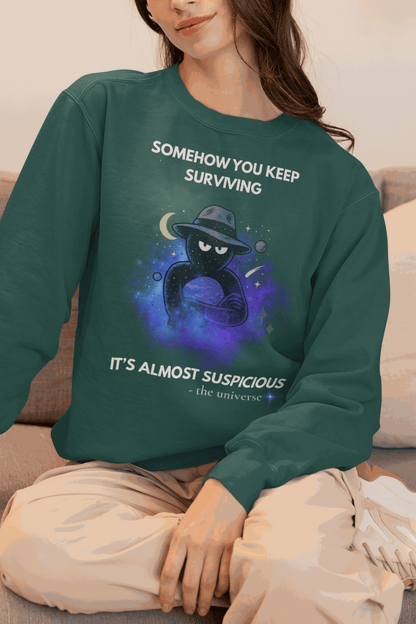 A dark green sweatshirt with a cosmic graphic and the text "Somehow you keep surviving it's almost suspicious".