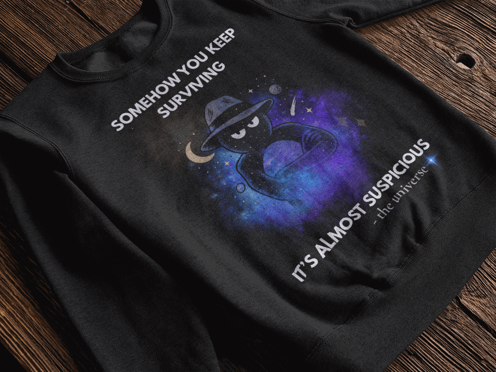 Black sweatshirt with a cosmic graphic and text that reads "Somehow you keep surviving" and "It's almost suspicious - the universe".