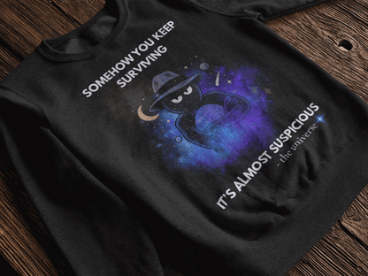 Black sweatshirt with a cosmic graphic and text that reads "Somehow you keep surviving" and "It's almost suspicious - the universe".