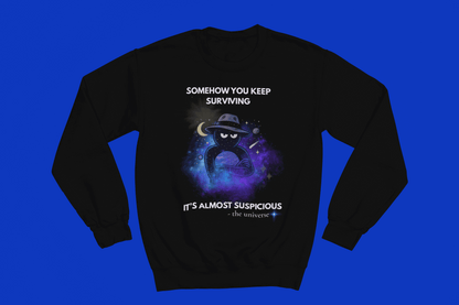 Black sweatshirt with a cosmic graphic and text "Somehow you keep surviving it's almost suspicious".