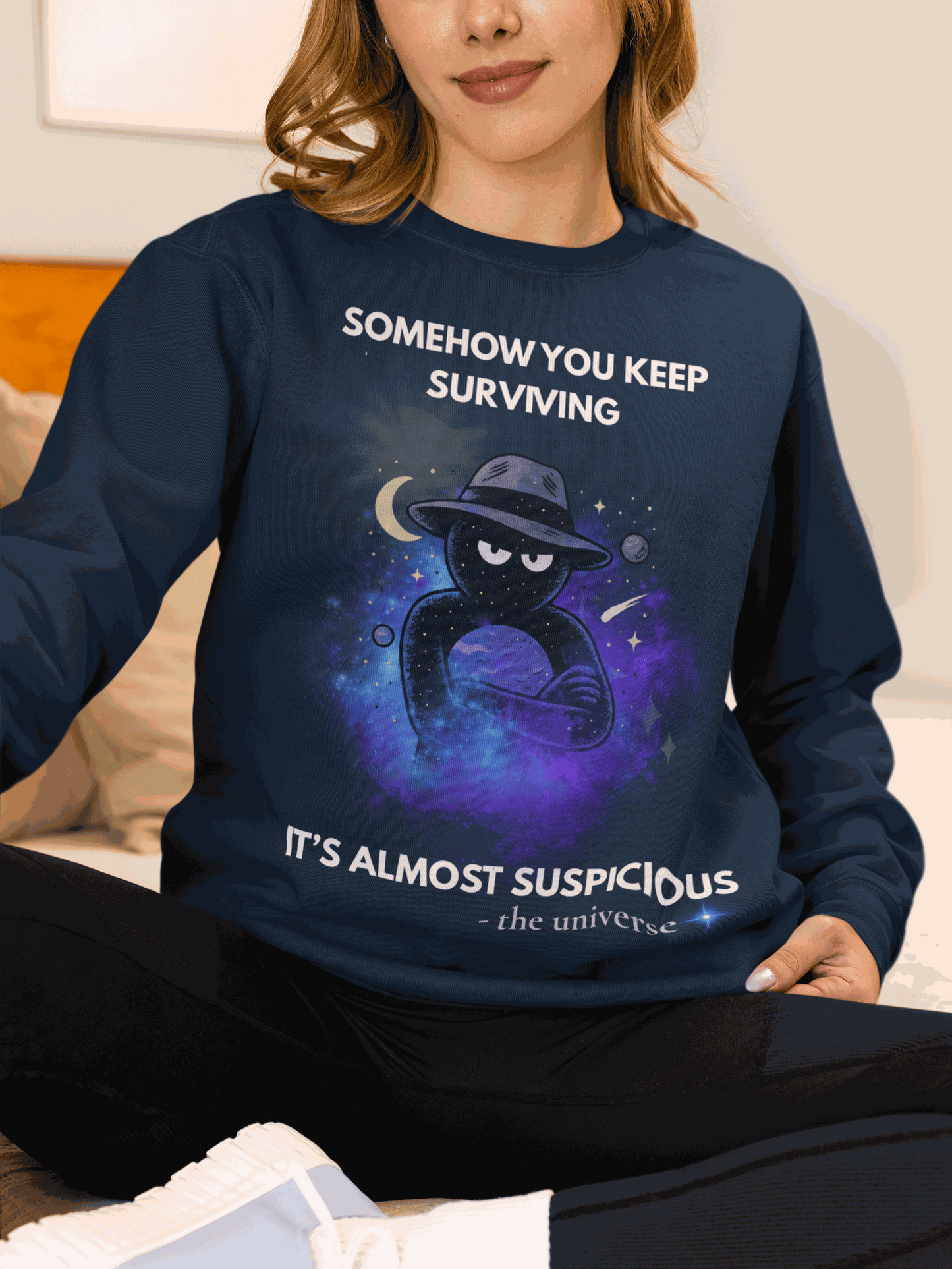 A navy sweatshirt with a cosmic graphic and the text "Somehow you keep surviving, it's almost suspicious".