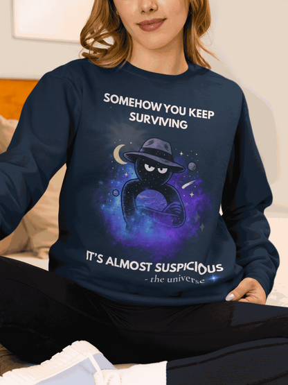 A navy sweatshirt with a cosmic graphic and the text "Somehow you keep surviving, it's almost suspicious".