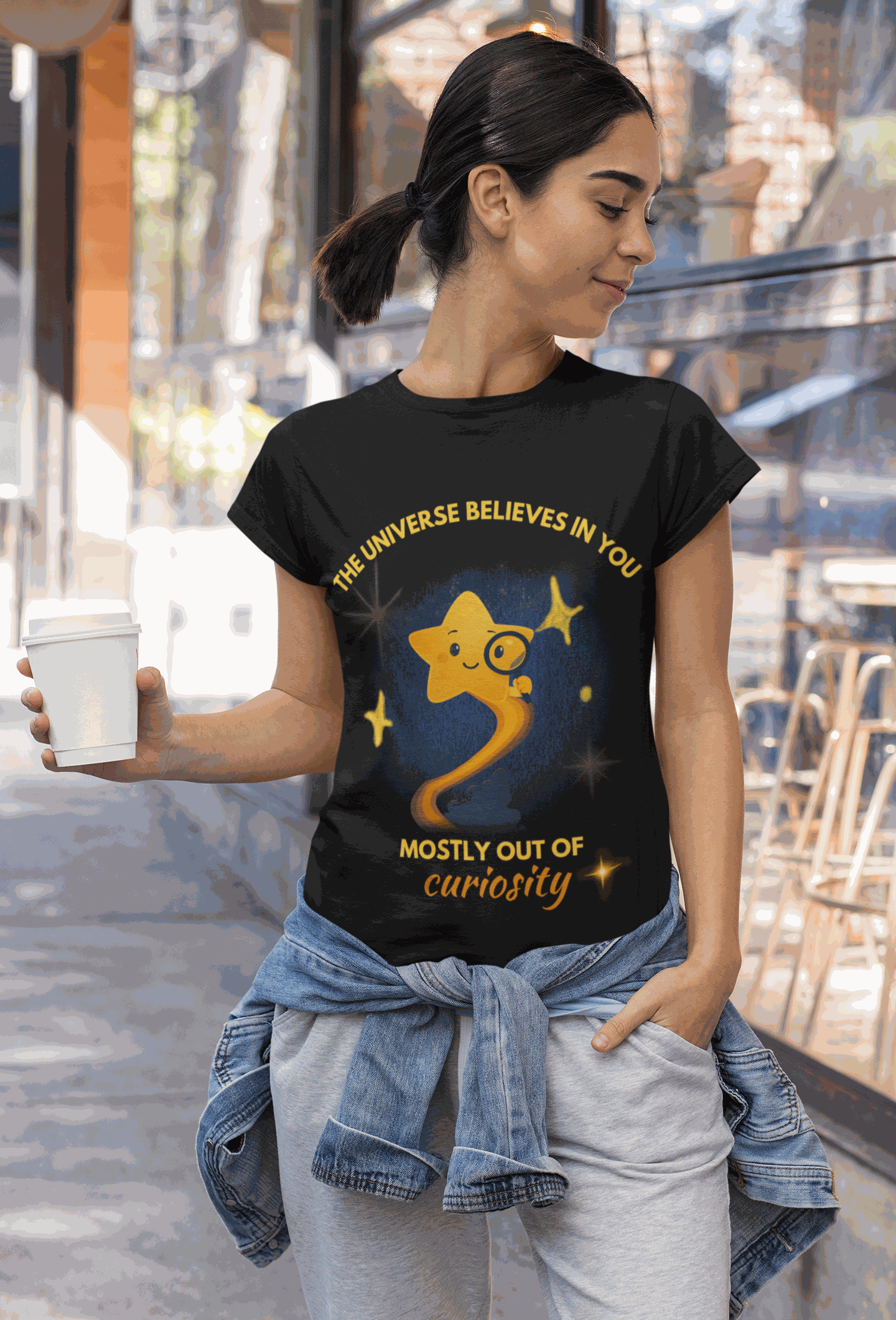 A woman wears a black t-shirt with a graphic of a star and the text "The Universe Believes in You Mostly Out of Curiosity".