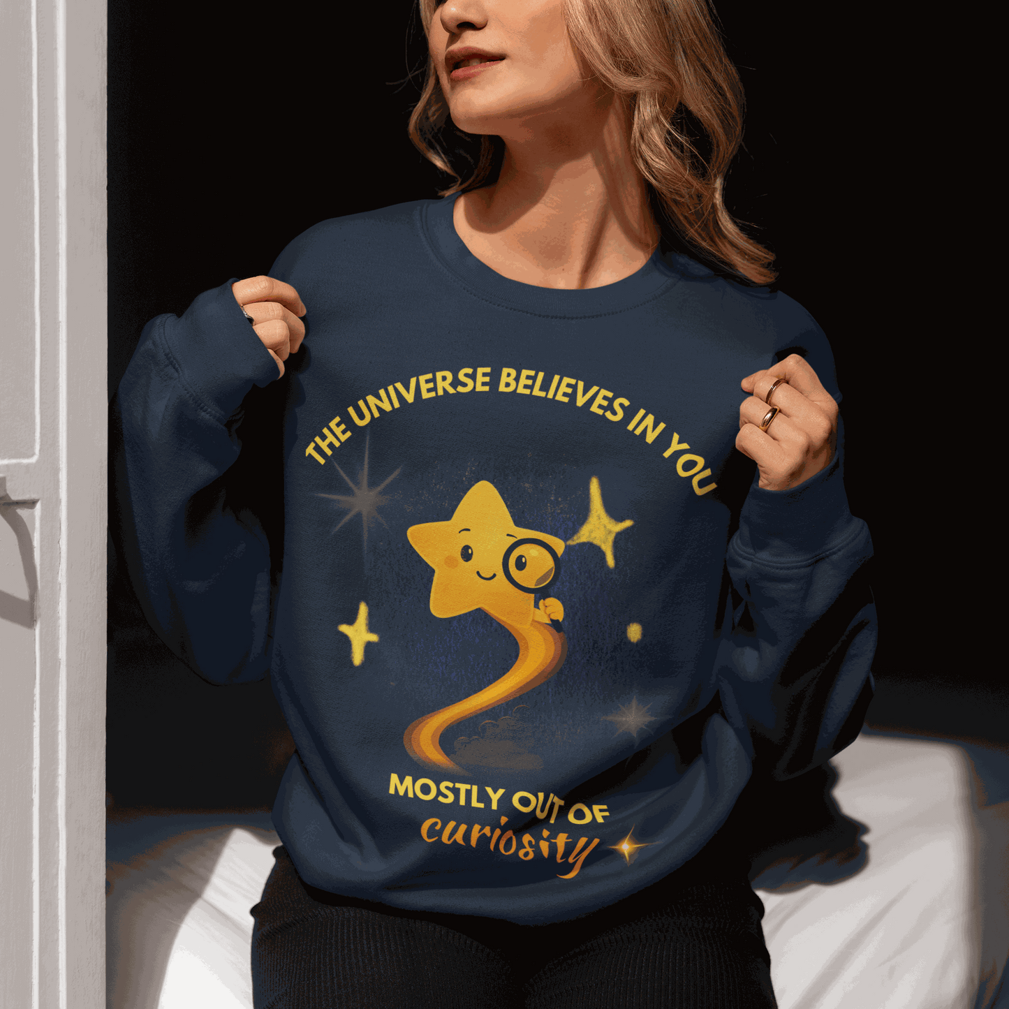 A navy sweatshirt with a graphic of a star and the text "The Universe Believes in You Mostly Out of Curiosity".
