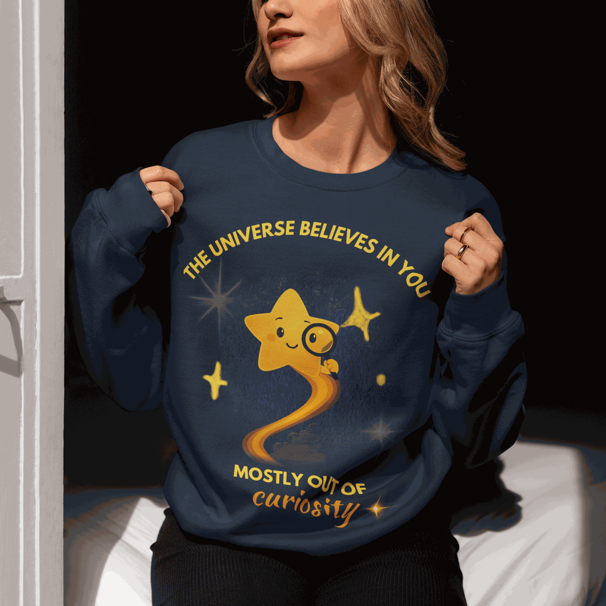 A navy sweatshirt with a graphic of a star and the text "The Universe Believes in You Mostly Out of Curiosity".
