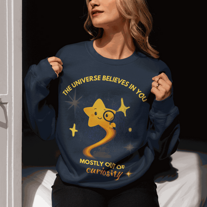 A navy sweatshirt with a graphic of a star and the text "The Universe Believes in You Mostly Out of Curiosity".