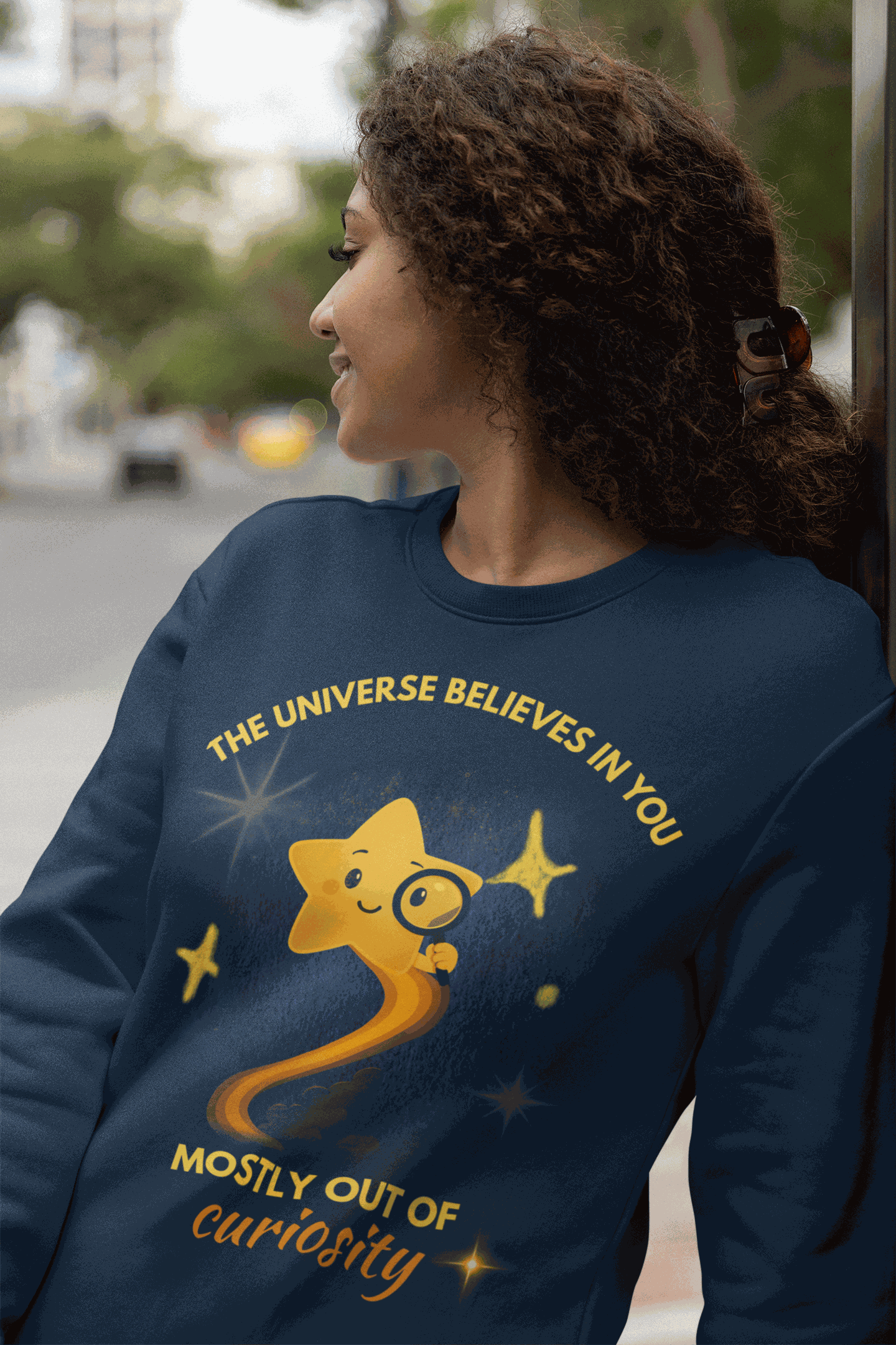 A navy sweatshirt with a graphic of a star and the text "The Universe Believes in You Mostly Out of Curiosity".