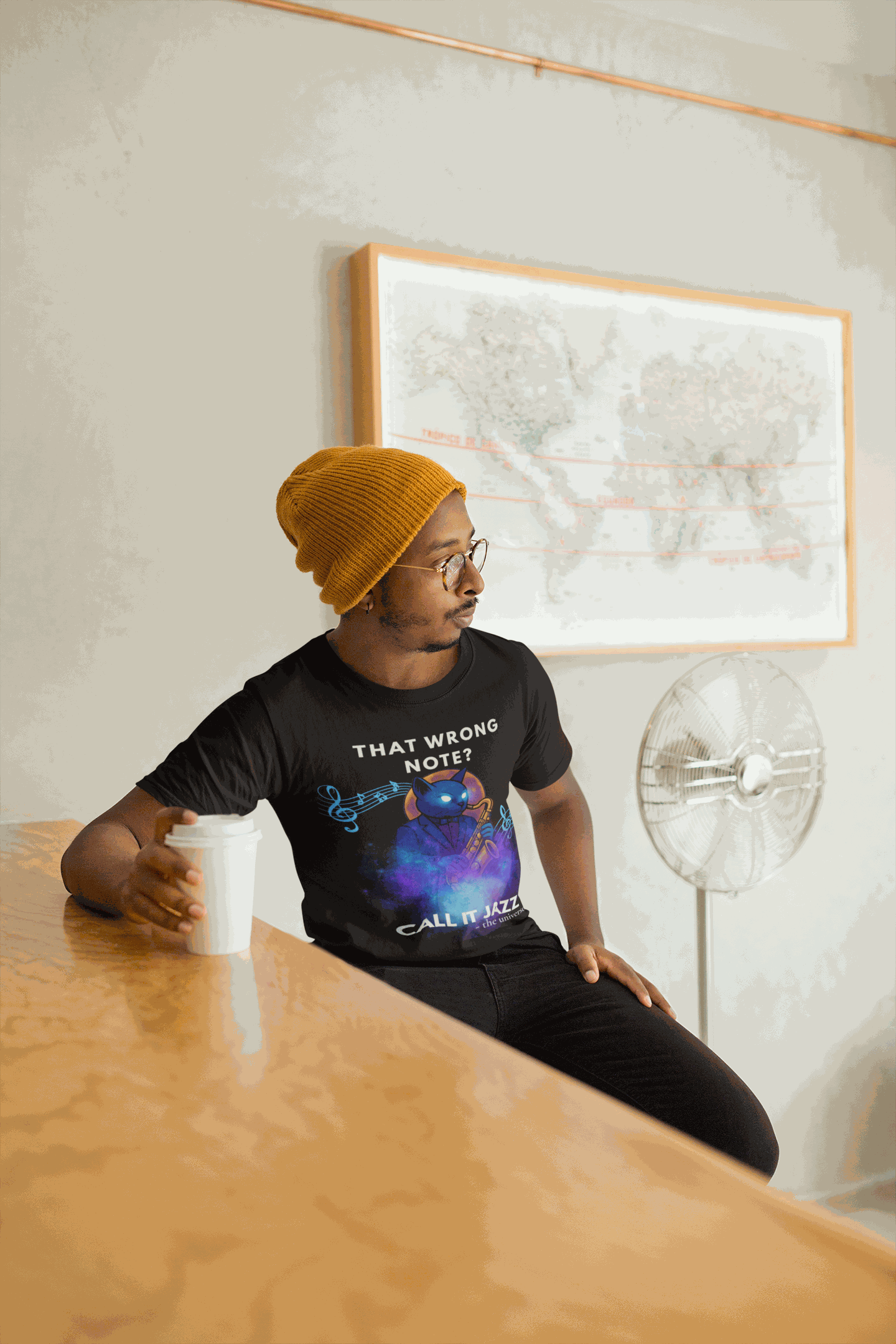 A man wears a black t-shirt with a cosmic cat playing a saxophone.