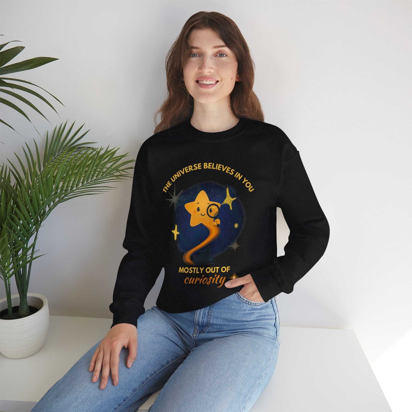 A woman wears a black sweatshirt with a graphic of a star and the text "The Universe Believes in You Mostly Out of Curiosity".