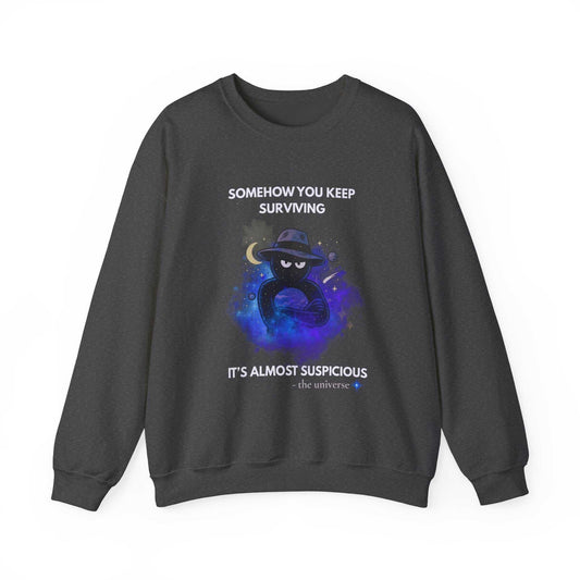 A dark grey sweatshirt with a graphic of a shadowy figure in a hat against a cosmic background and text that reads "Somehow you keep surviving it's almost suspicious".