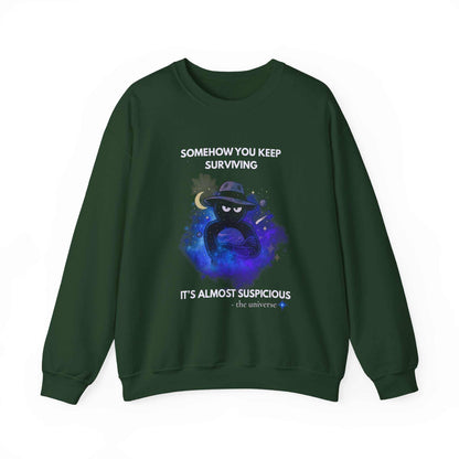 A dark green sweatshirt with a graphic of a figure in a hat in space and text that reads "Somehow you keep surviving. It's almost suspicious - the universe."