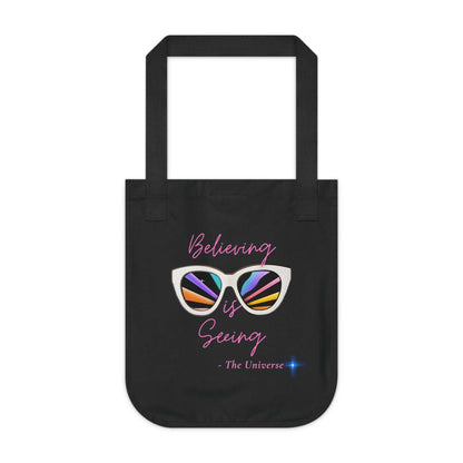 Black organic canvas tote bag with "Believing is Seeing" sunglasses graphic and long handles