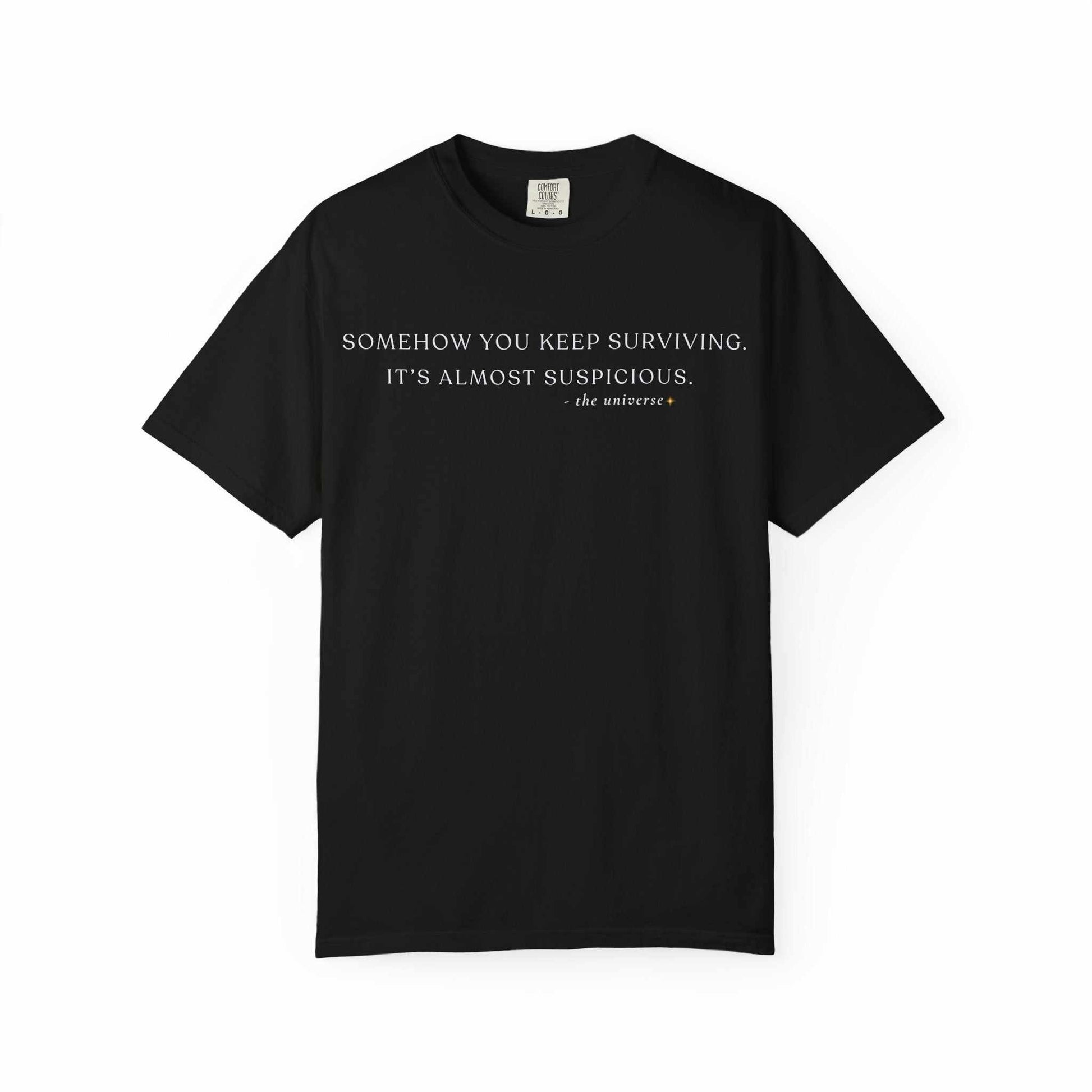 Black Comfort Colors t-shirt with 'Somehow you keep surviving. It's almost suspicious.' quote in white text.